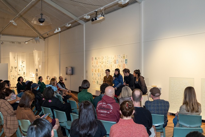 Image of panel in gallery with art works behind them and audience in front.