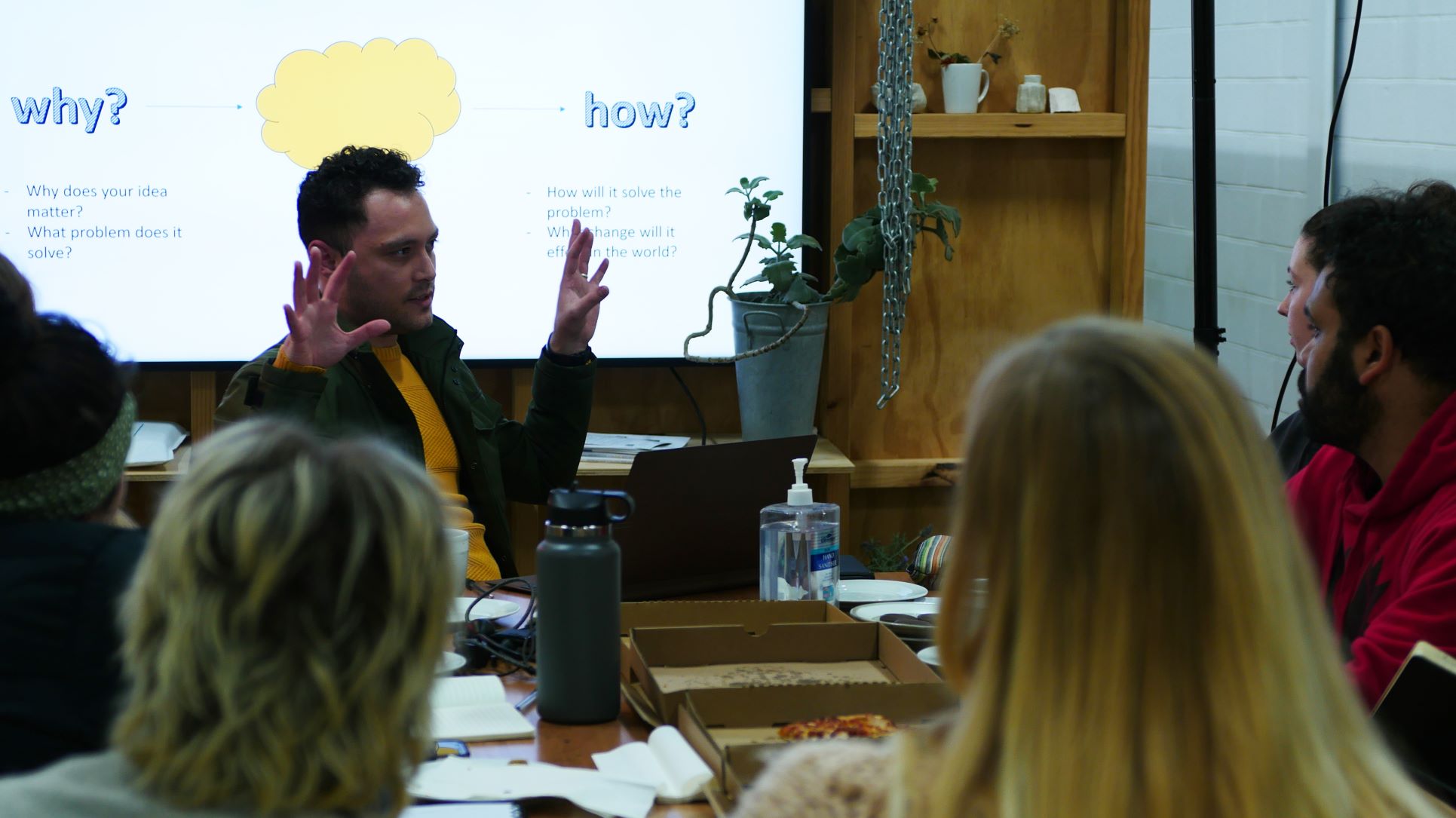 Man sitting behind a table speaking to a group of young creative makers at 'Make it happen' workshop