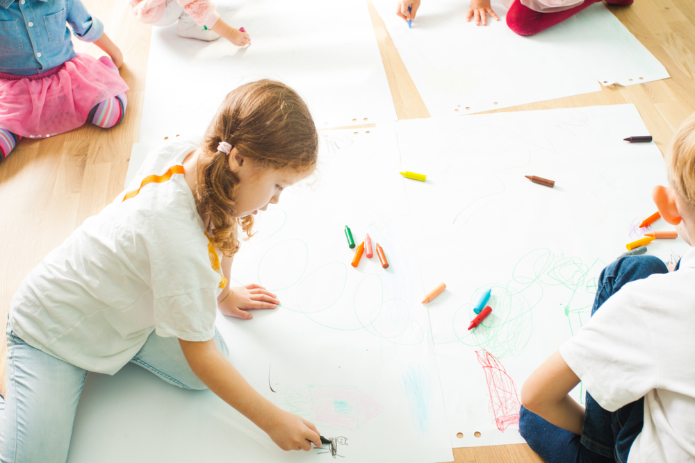 Group of young children on the floor drawing on large sheets of white paper